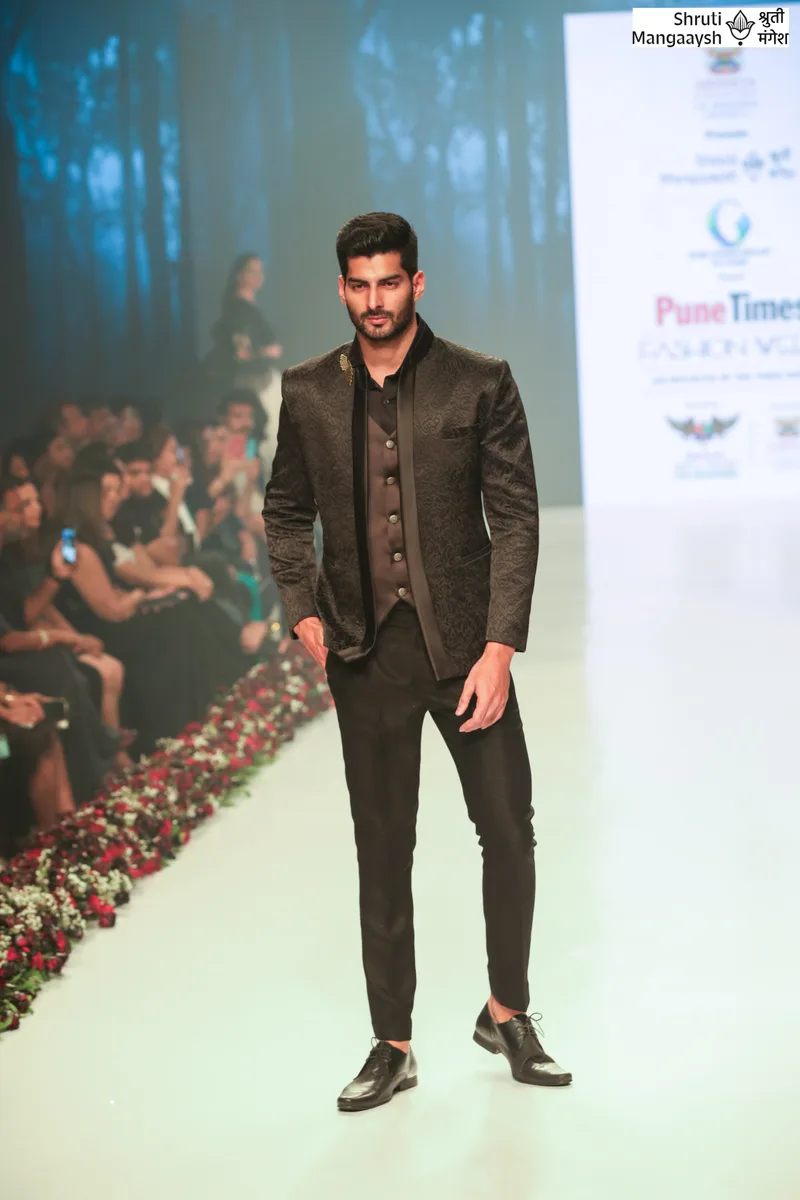 Model wearing a black embroidered jacket and black trousers on the runway