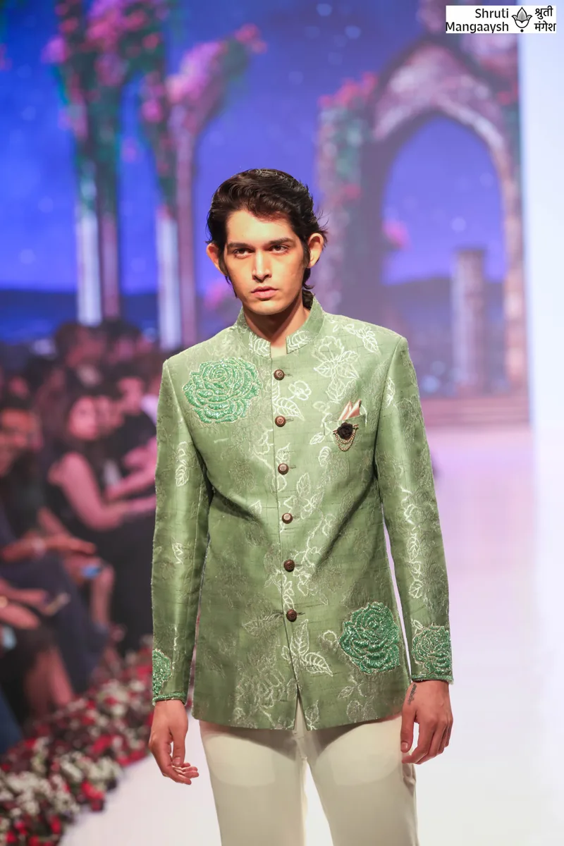 Model wearing a green brocade jacket with pale trousers