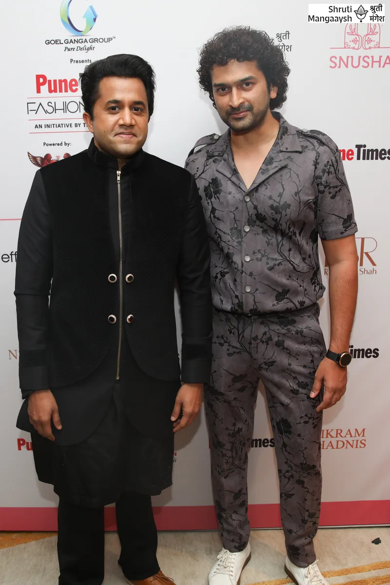 Two men posing backstage in black and grey outfits