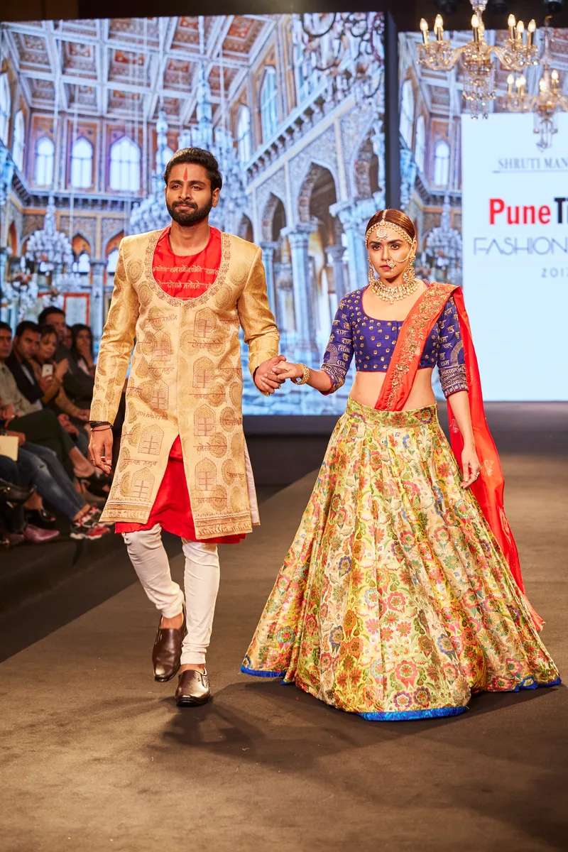 Two models wearing a gold sherwani and a floral lehenga