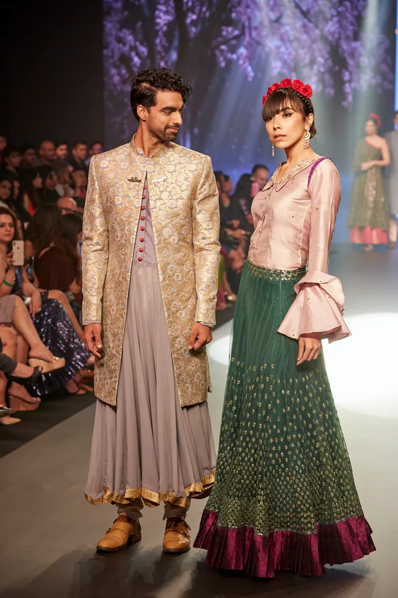 Two models wearing a grey embroidered jacket and a green skirt with pink top