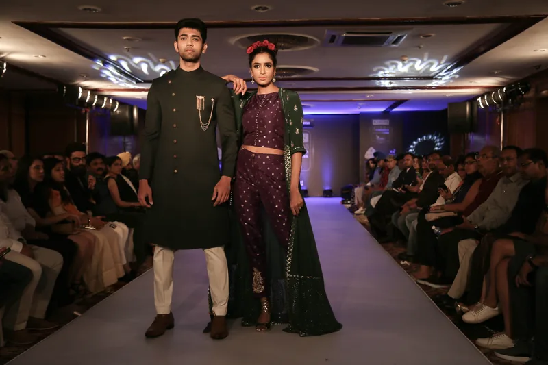 Two models wearing dark embroidered outfits on an indoor runway