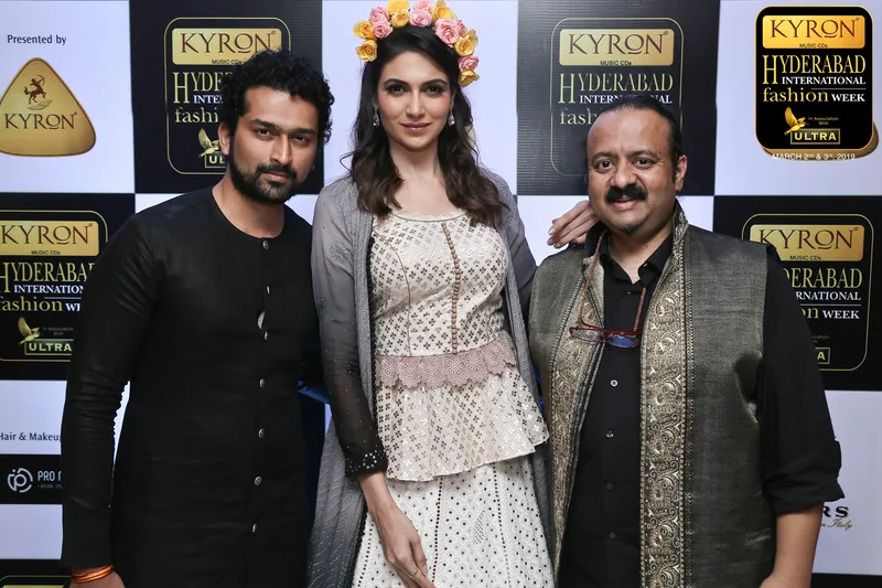 Three people posing at a fashion event photo backdrop