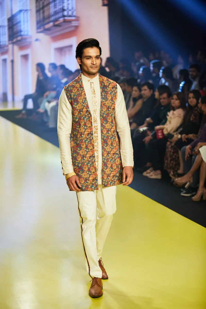 Model wearing a patterned waistcoat over an ivory kurta set