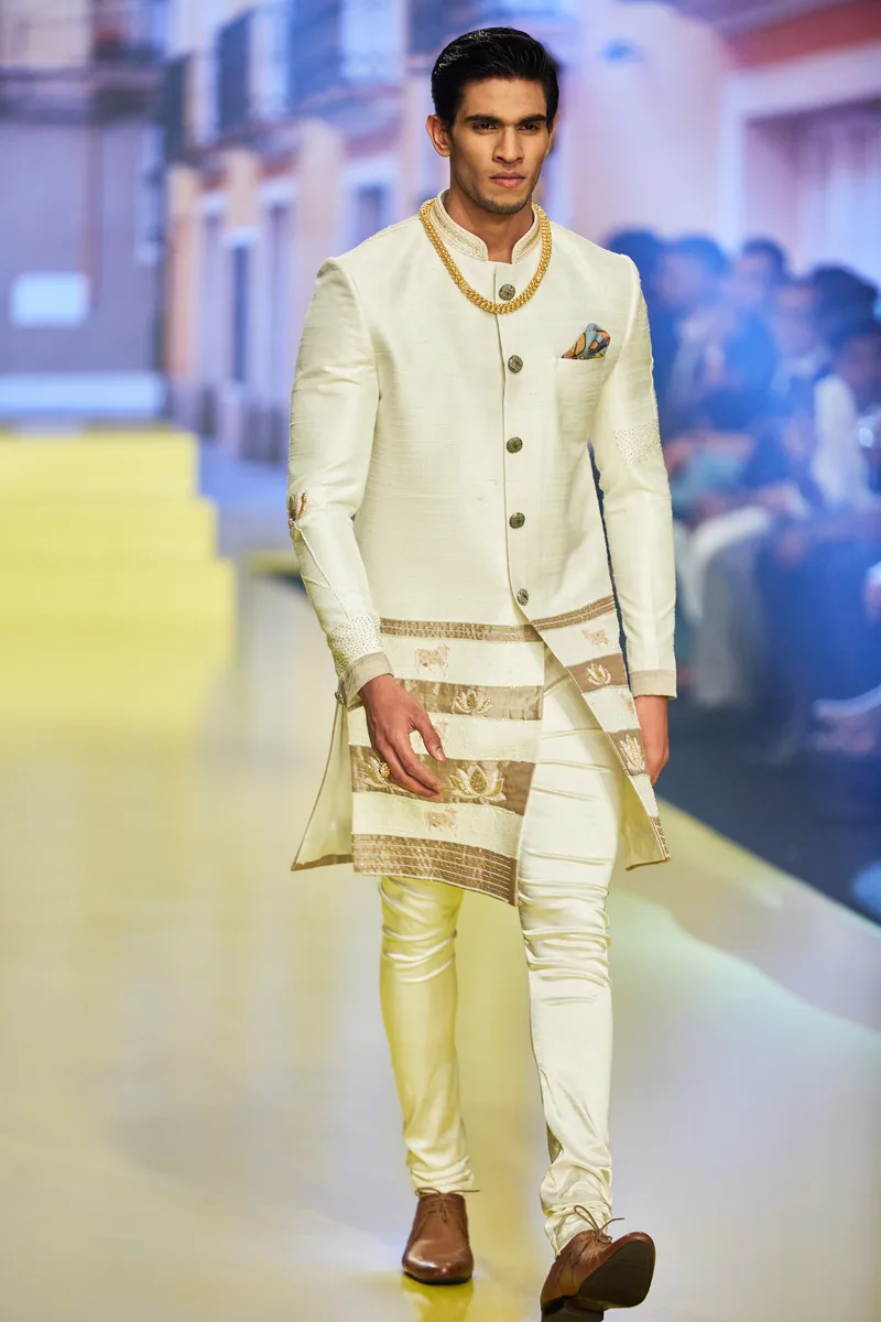 Model wearing a pale green sherwani with red and gold borders