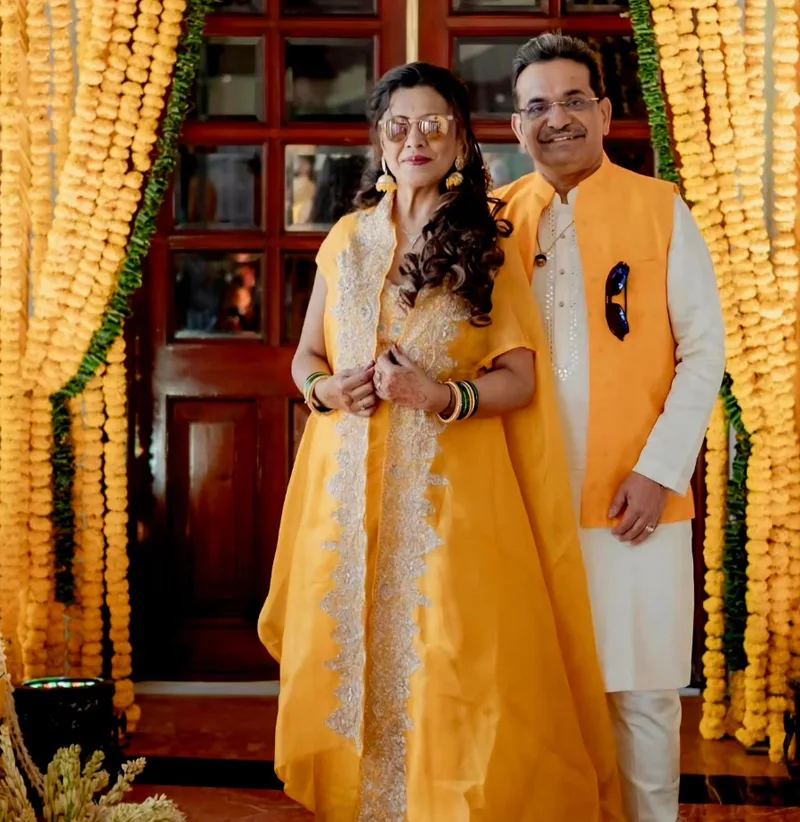 Couple posing together in yellow and white outfits beside marigold garlands
