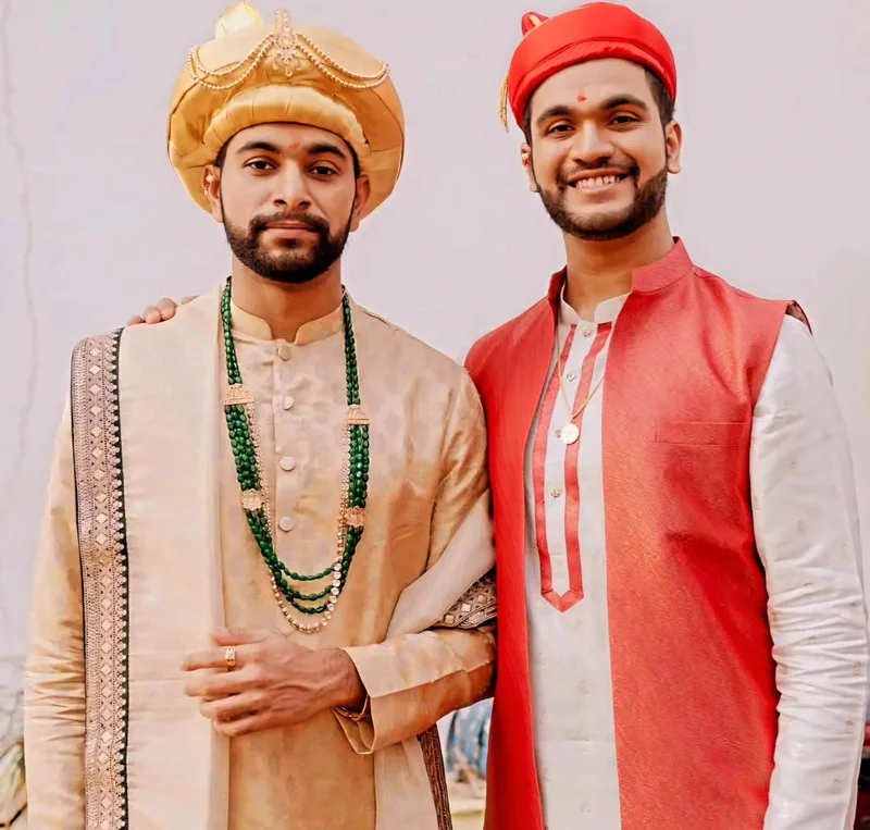 Two men wearing ivory kurtas with gold and red waistcoats and turbans
