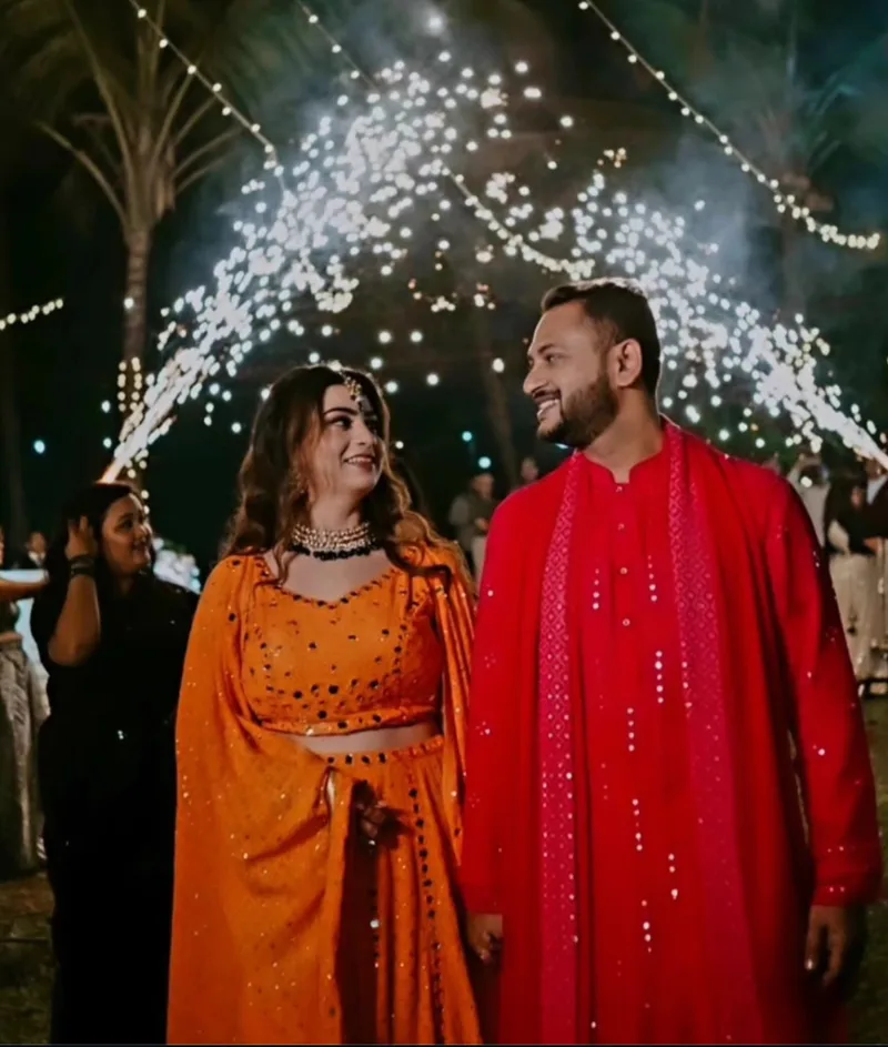 Couple in orange and red outfits beneath sparkling lights