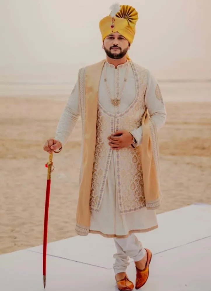 Groom wearing an ivory sherwani and gold turban, holding a ceremonial sword